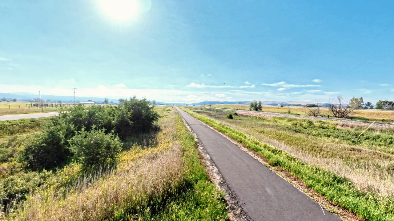 A paved trail running straight through grassland toward distant mountains, 2026