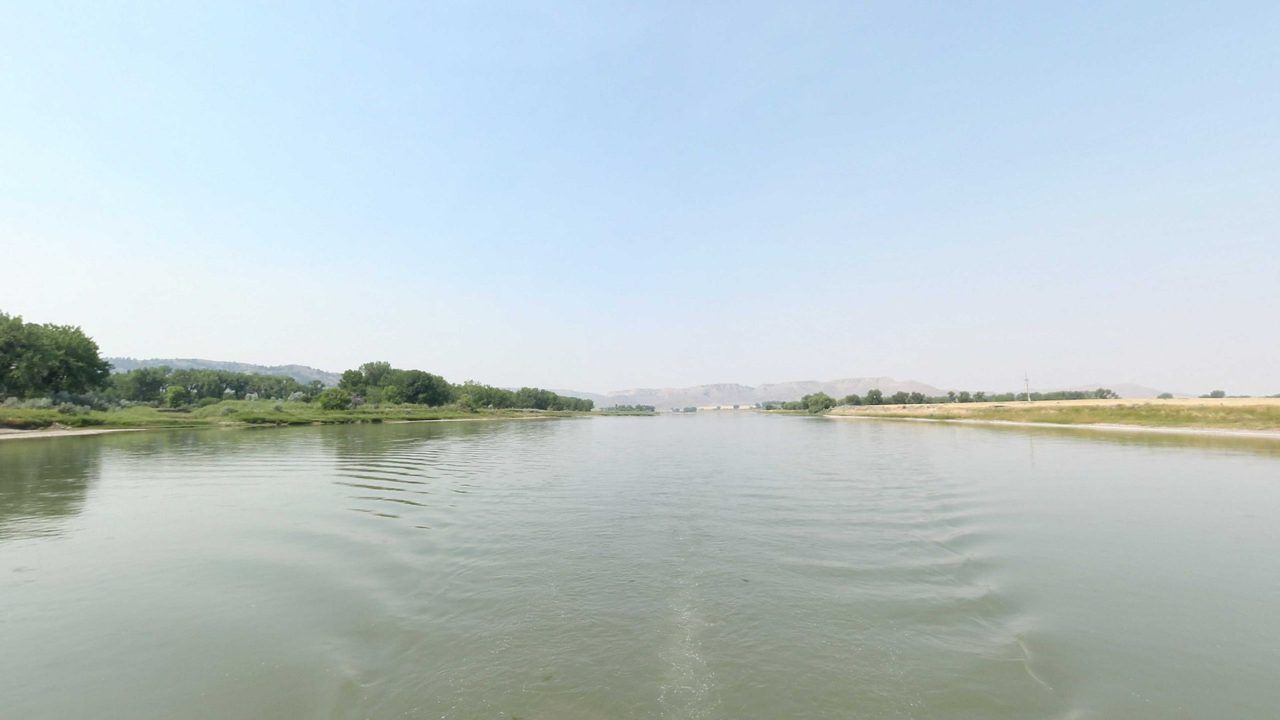 The Missouri River between a wooded bank and open grassland, with hazy bluffs in the distance, 2021