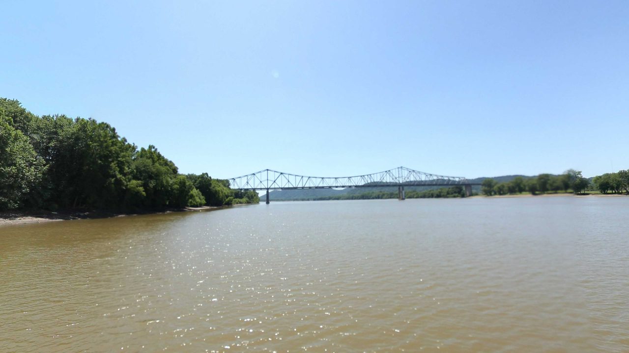 The Ohio River beside a wooded bank, with a long truss bridge downstream, 2022