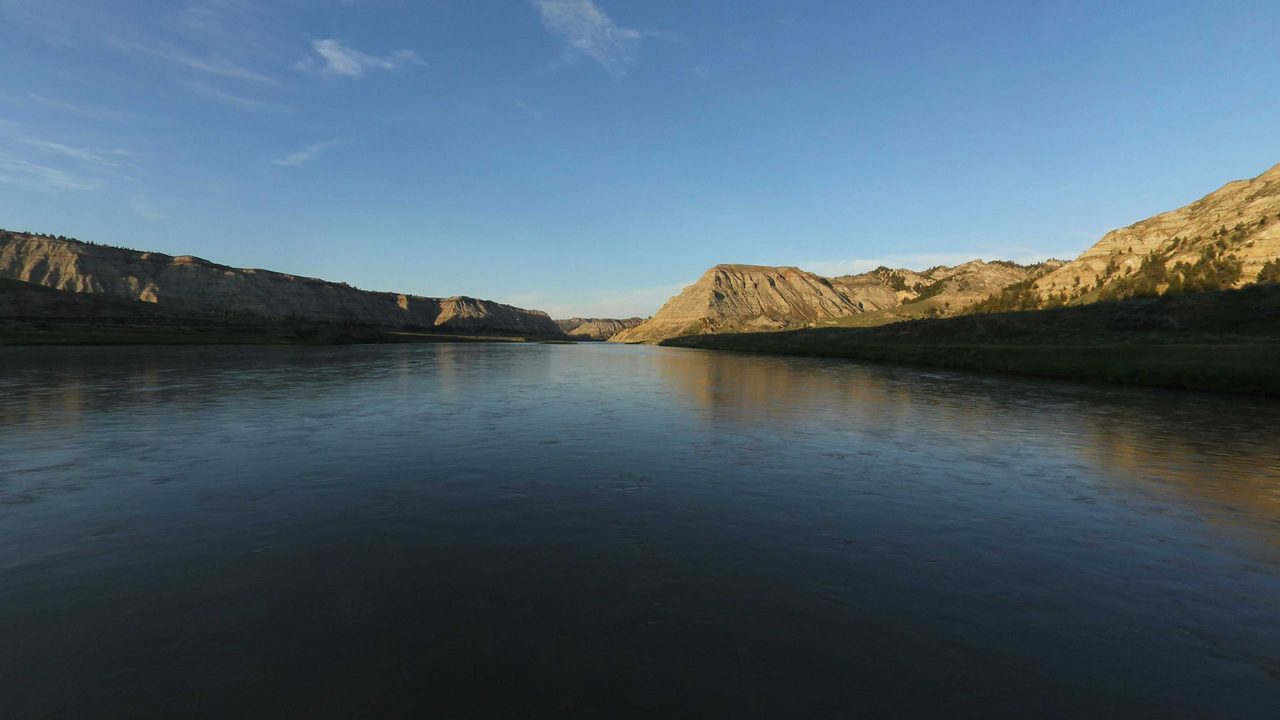 The Missouri River between tall badland bluffs under a clear sky, 2022