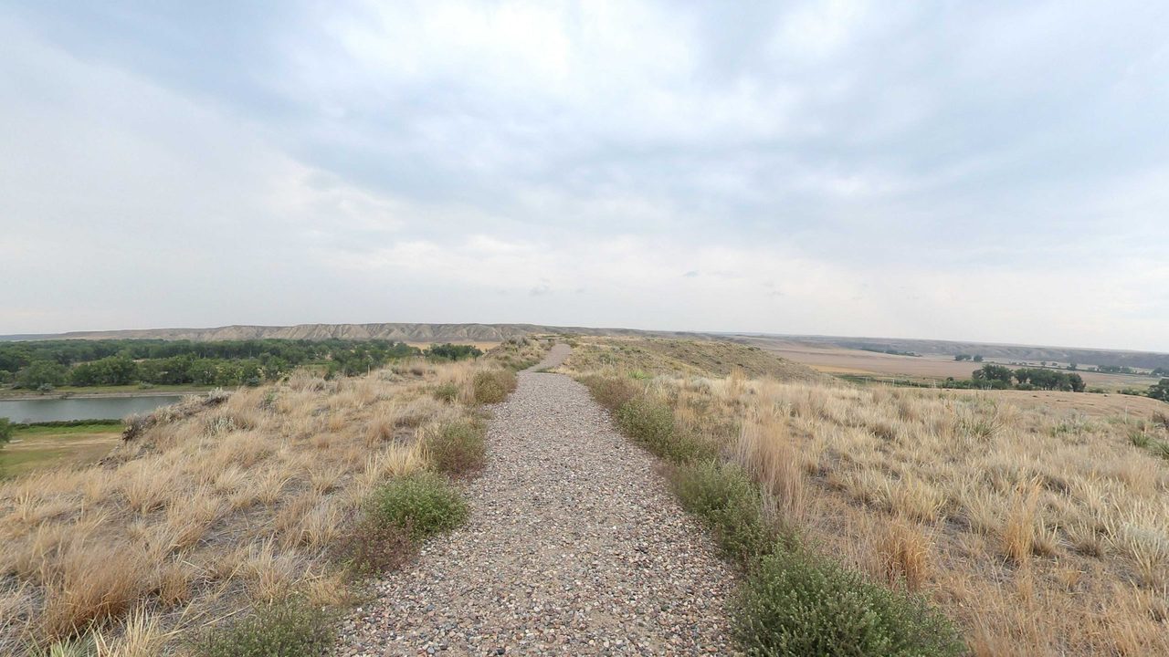 A gravel footpath along a grassy bluff, with a river and wooded bottomland below on the left, 2022