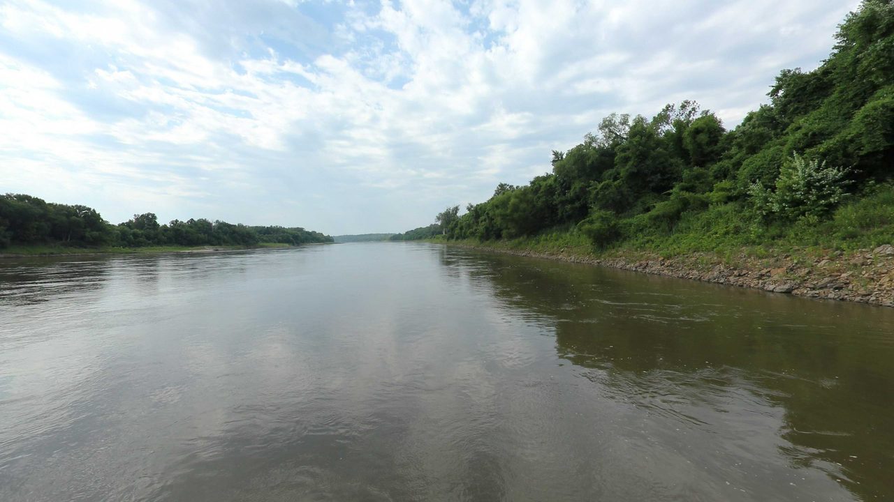 The wide Missouri River between wooded banks under scattered clouds, 2023