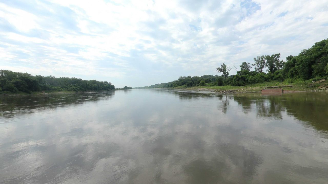 The Missouri River reflecting a cloudy sky between wooded banks, 2023