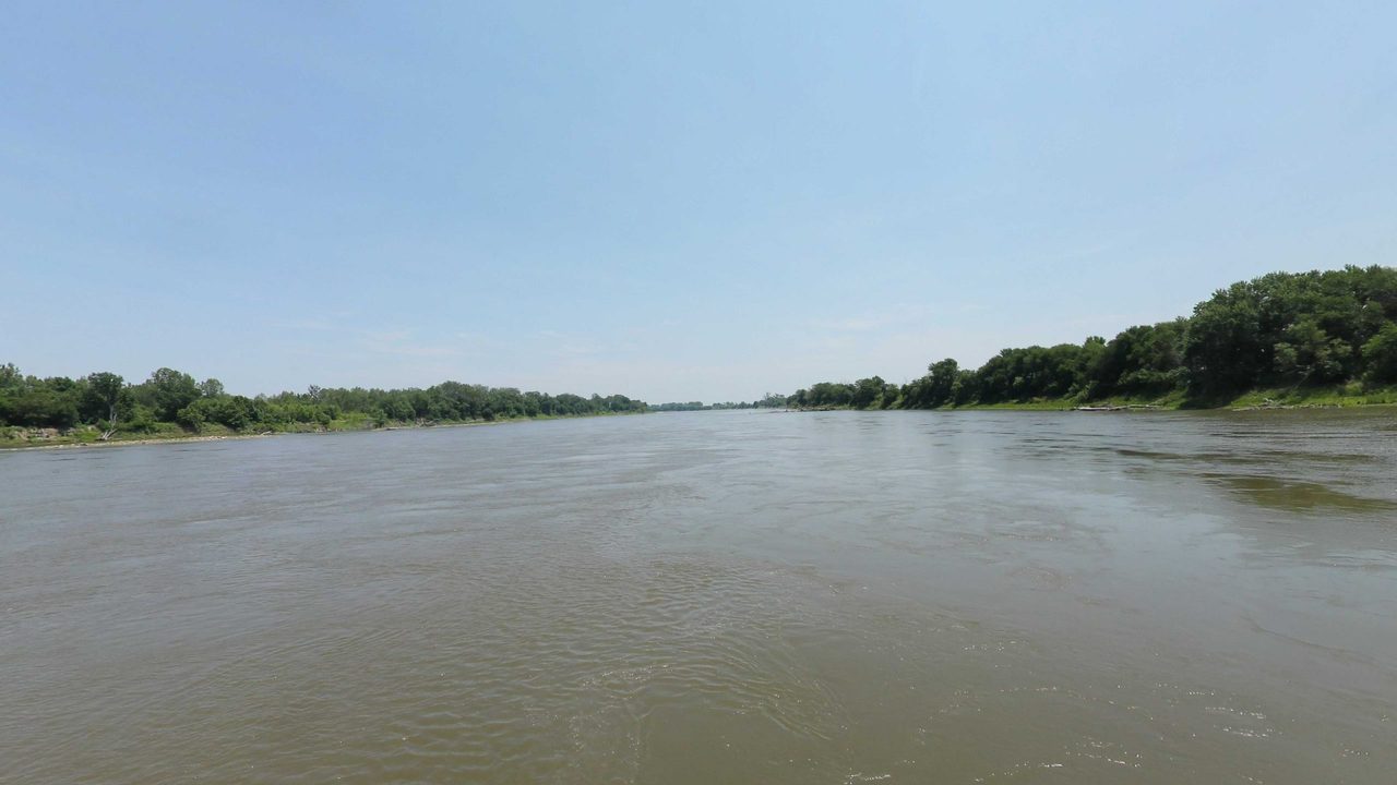 The wide Missouri River between low wooded banks, 2023
