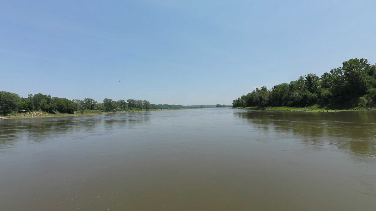 The wide Missouri River between wooded banks under a clear sky, 2023