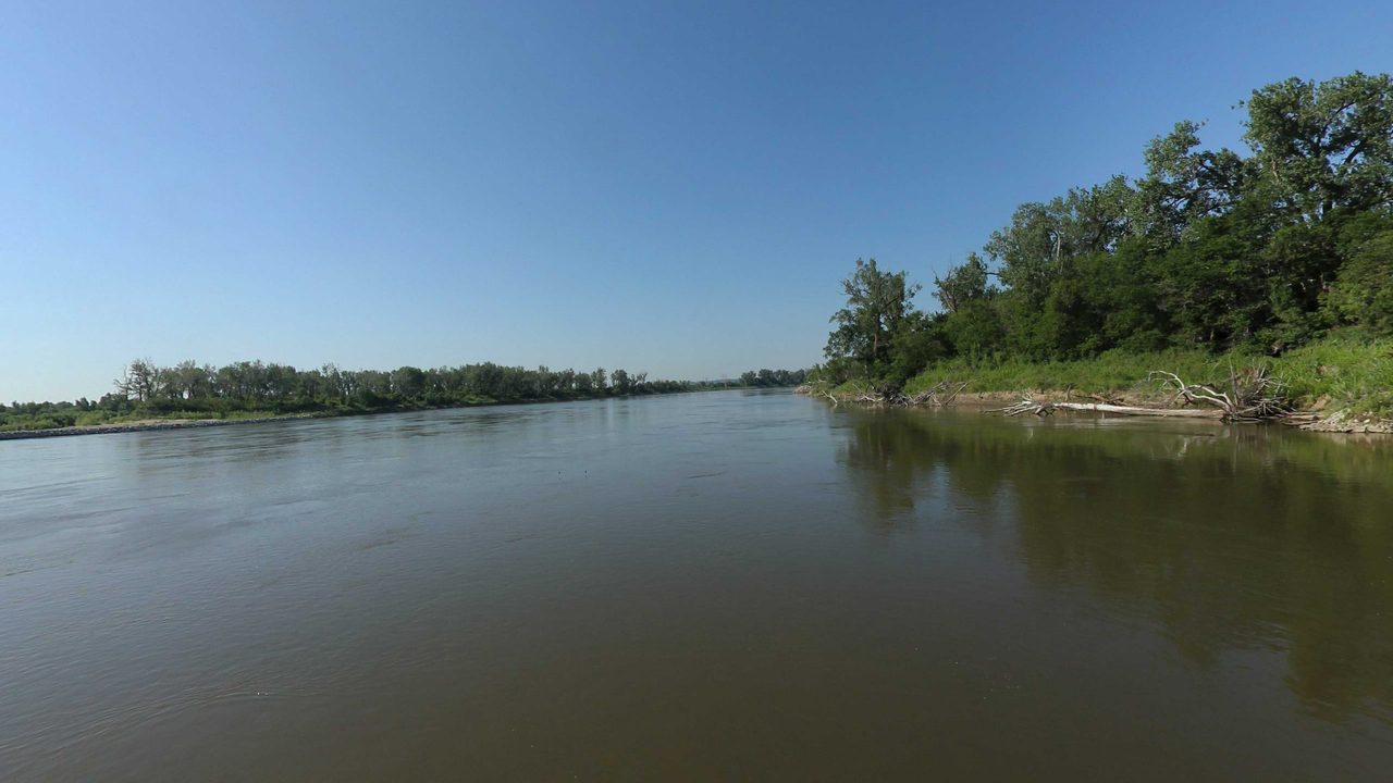 The calm Missouri River reflecting a wooded point on the right, 2023