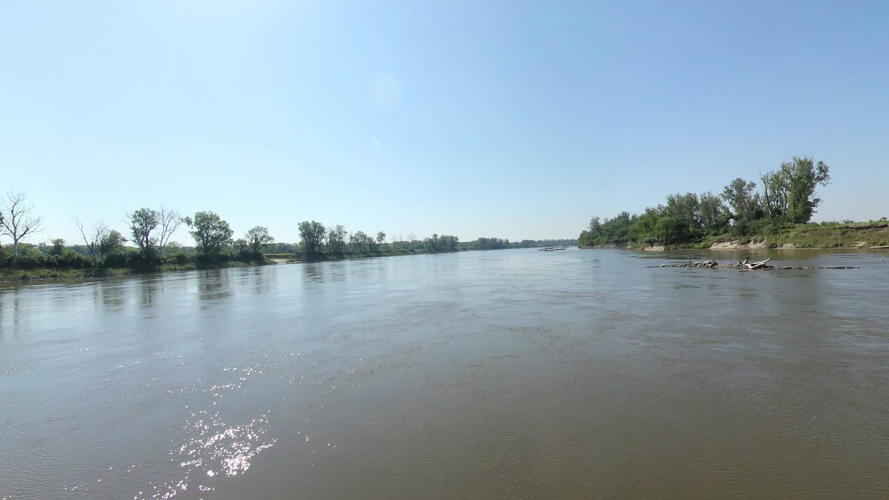 The Missouri River between low wooded banks, with sunlight glinting on the water, 2023