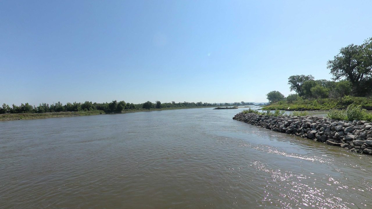 The Missouri River beside a rock dike reaching out from the wooded right bank, 2023