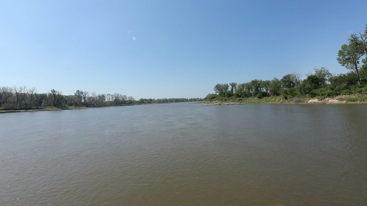 The Missouri River between tree-lined banks under a clear blue sky, 2023