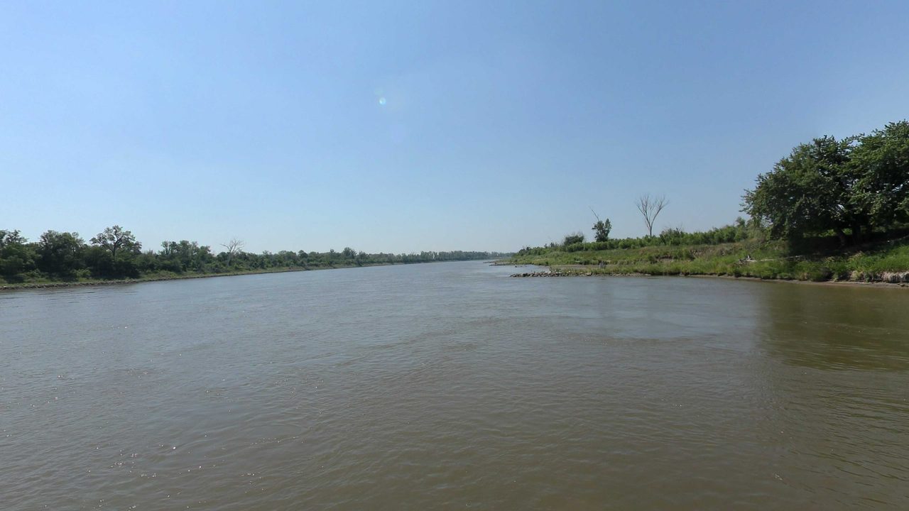 The Missouri River between low wooded banks under a clear blue sky, 2023