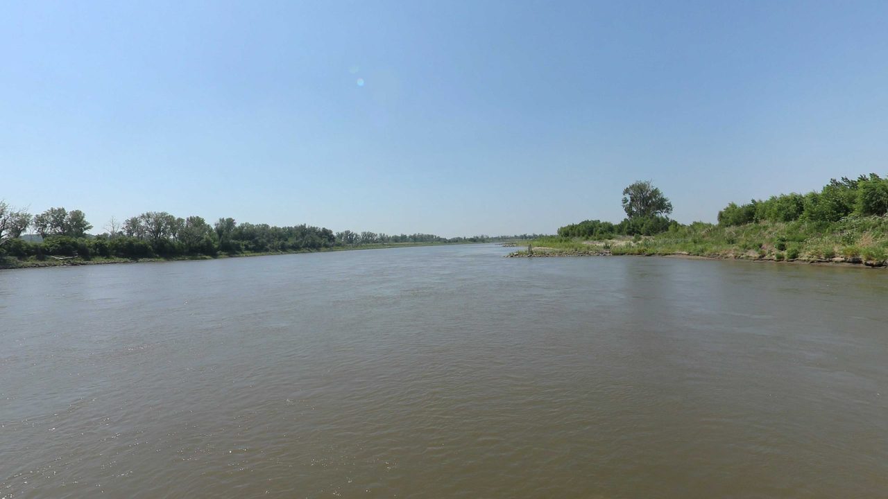 The Missouri River between long, low wooded banks under a clear sky, 2023