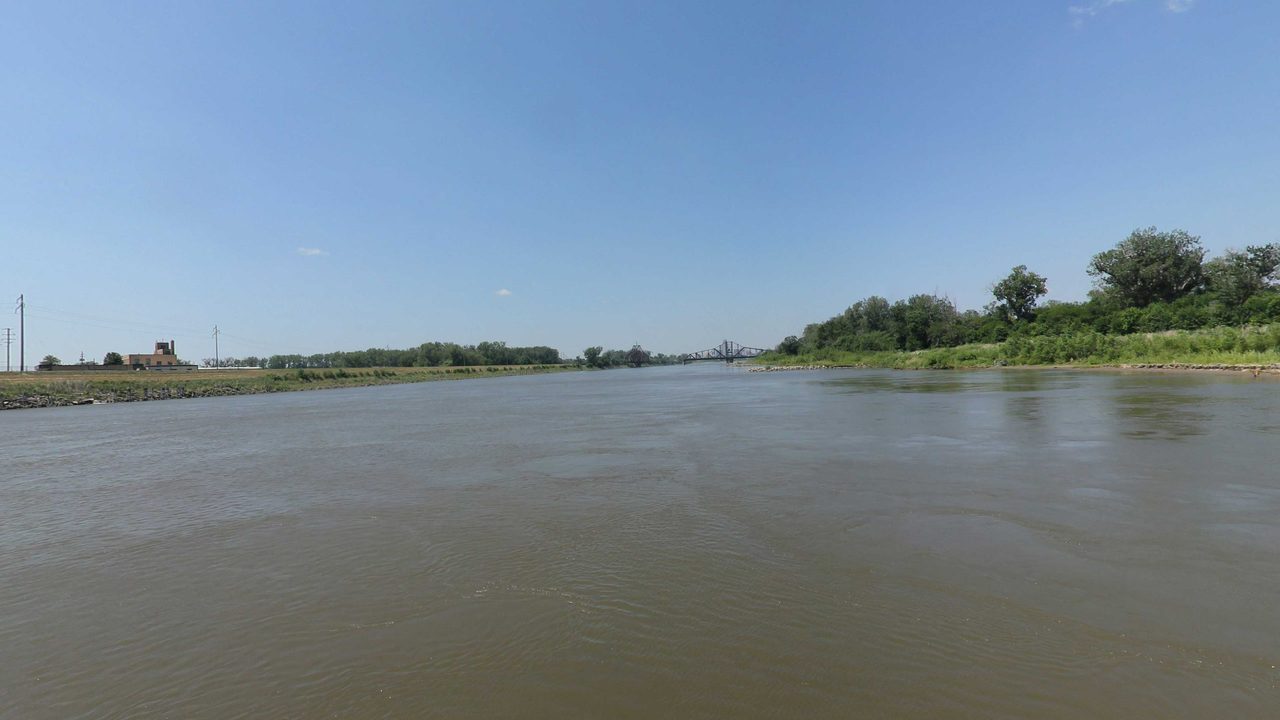 The Missouri River with a truss bridge in the distance and a wooded bank, 2023