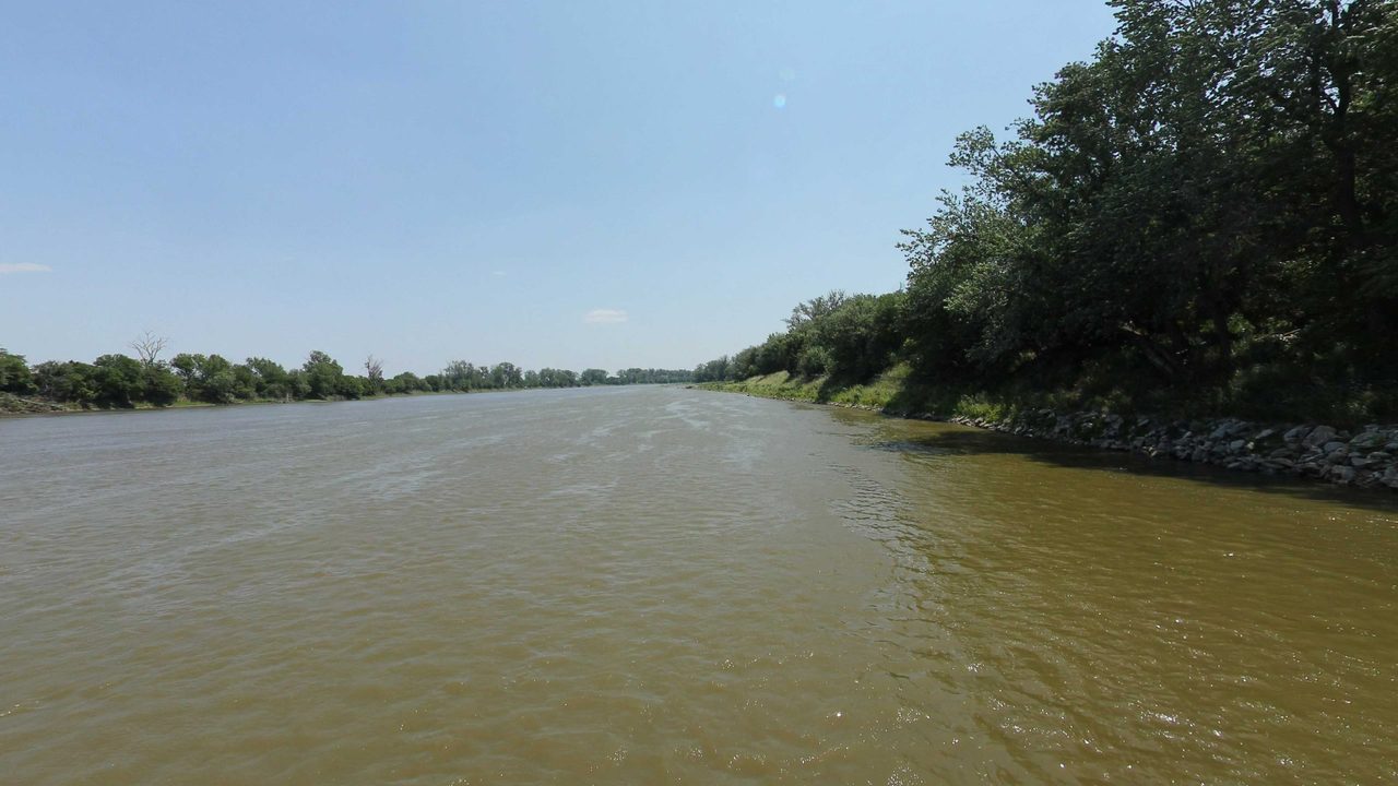 The Missouri River bending past a wooded bank lined with rocks, 2023