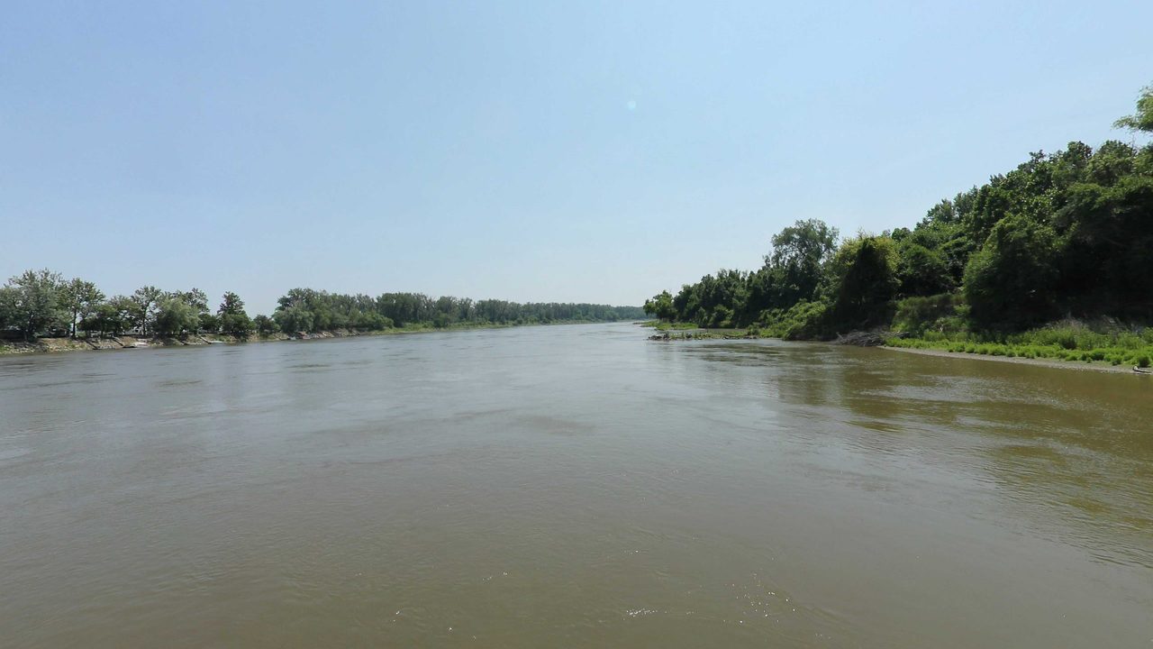 The Missouri River beside a densely wooded bluff, 2023