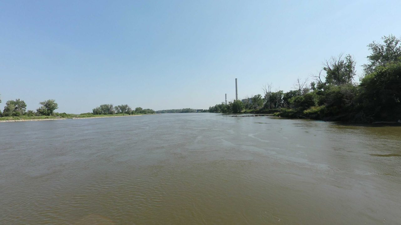 The Missouri River toward a distant smokestack, with a wooded bank on the right, 2023