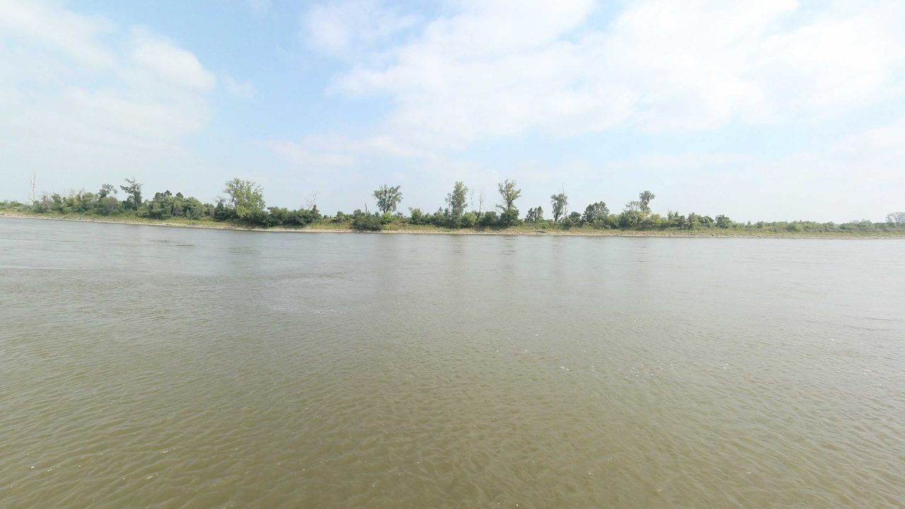 The wide Missouri River under a hazy sky, with a long, low wooded shore, 2023