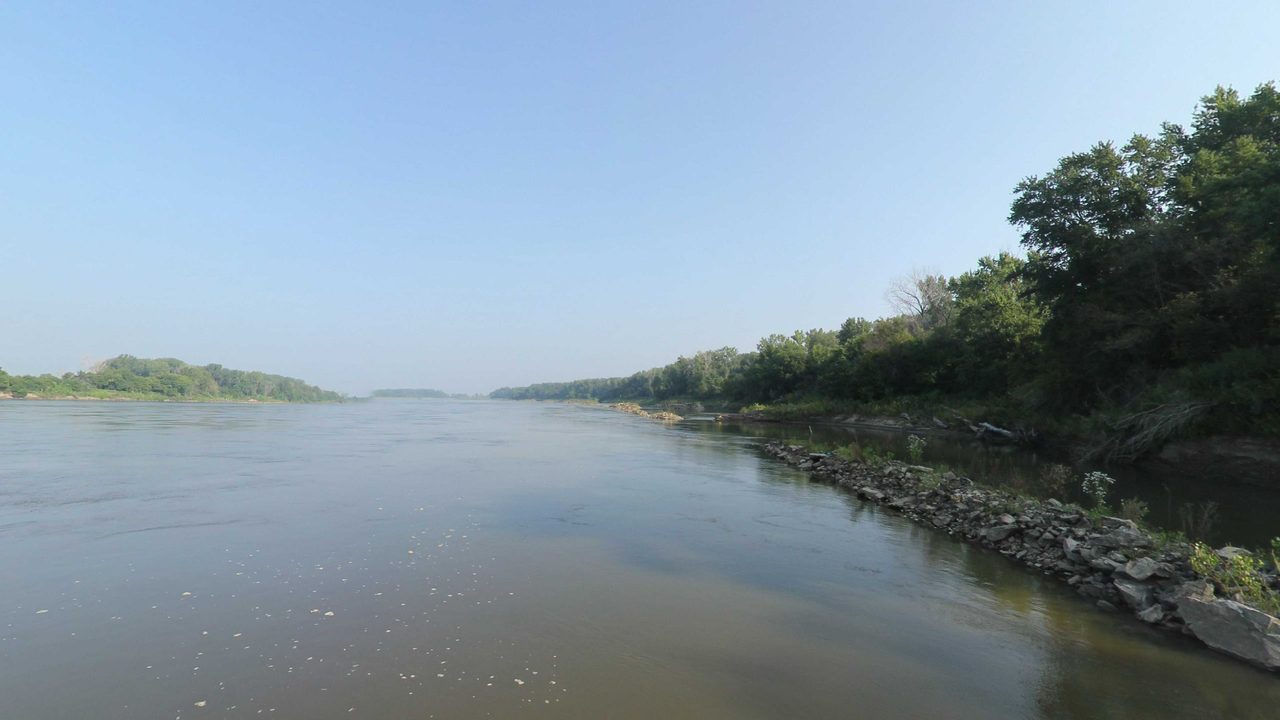 The Missouri River beside a rocky, wooded bank on the right, 2023