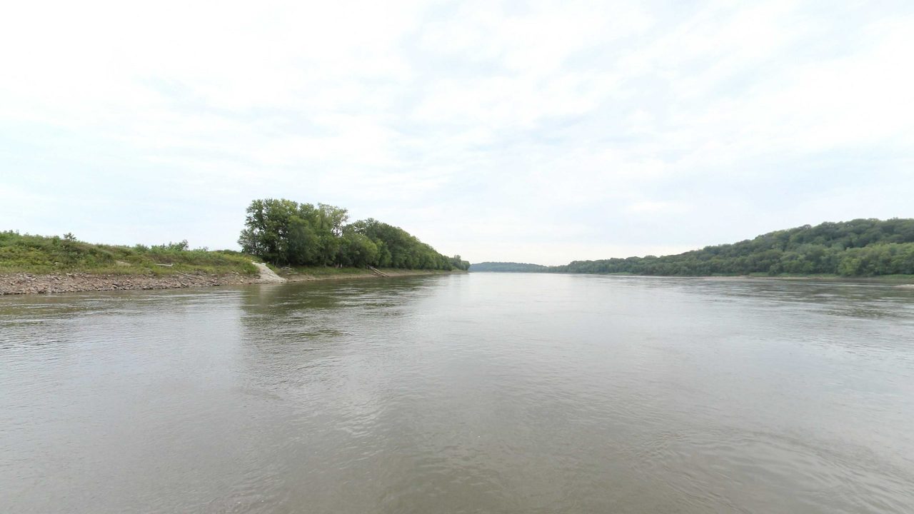 The Missouri River with a wooded point on the left and a low wooded shore across the water, 2023