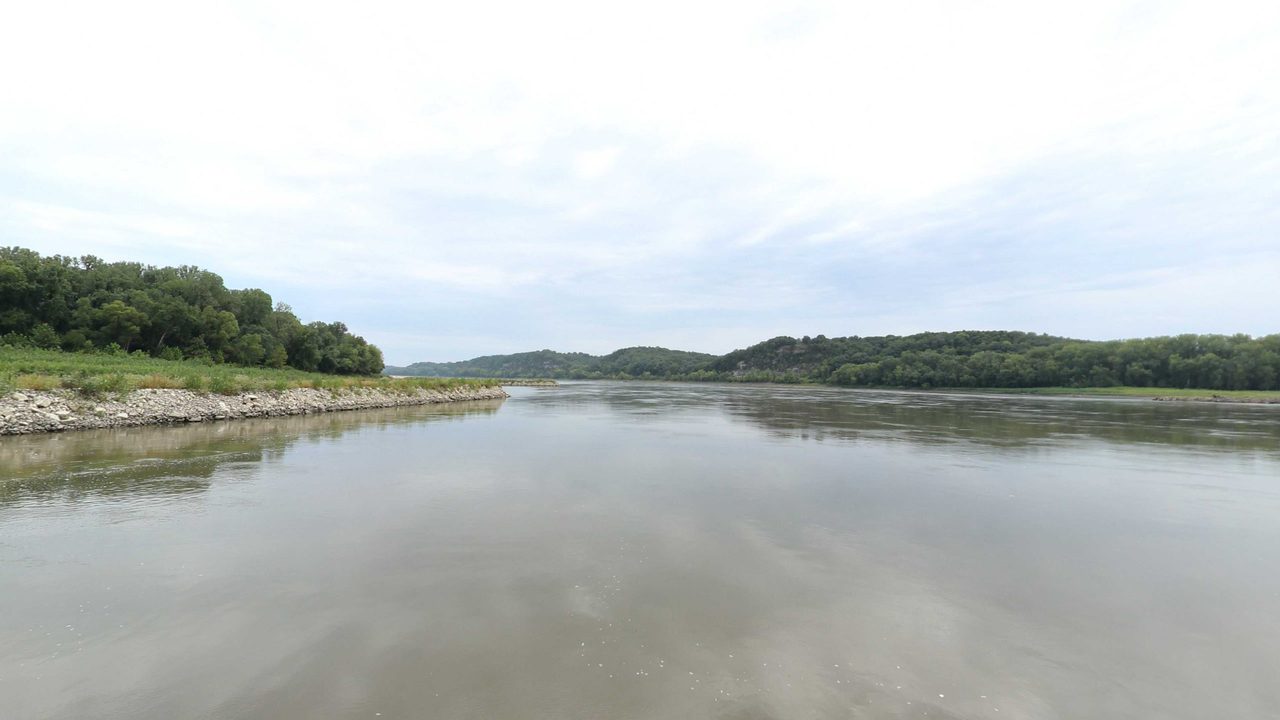 The Missouri River below wooded bluffs under an overcast sky, 2023
