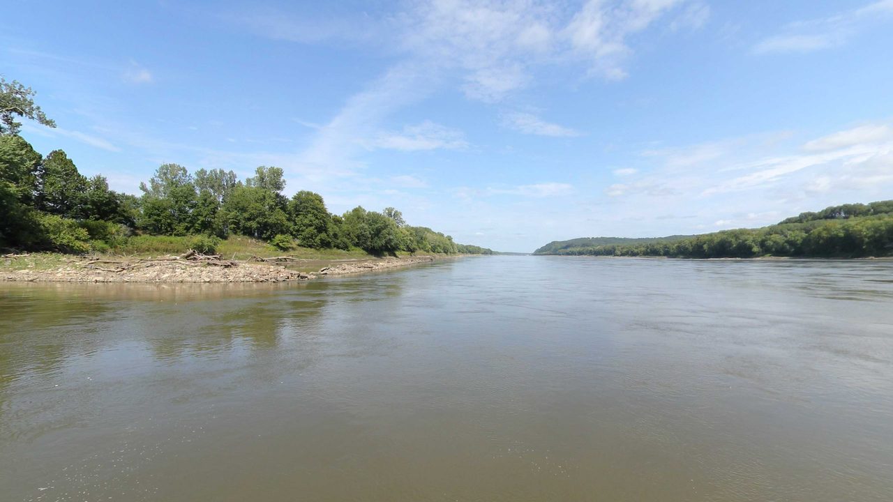 The Missouri River between a wooded point and distant bluffs under a blue sky, 2023