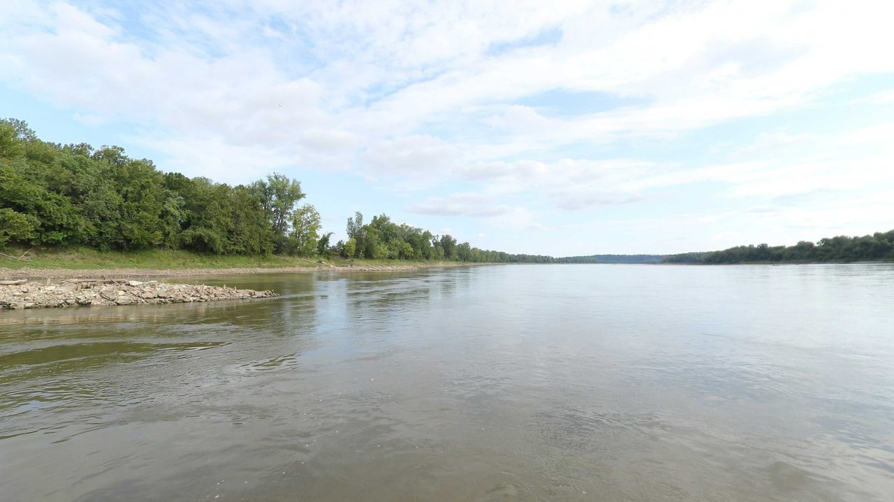 The wide Missouri River with a sandbar below the wooded left bank, 2023