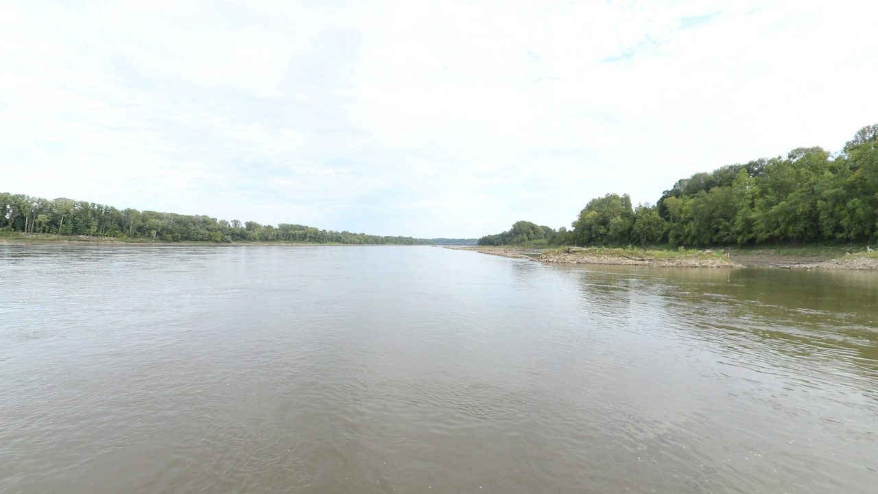 The Missouri River under an overcast sky, with a wooded point and a rocky bar on the right, 2023