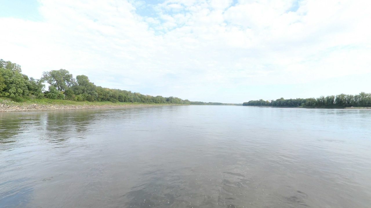 The Missouri River between low wooded banks under a sky of white clouds, 2023