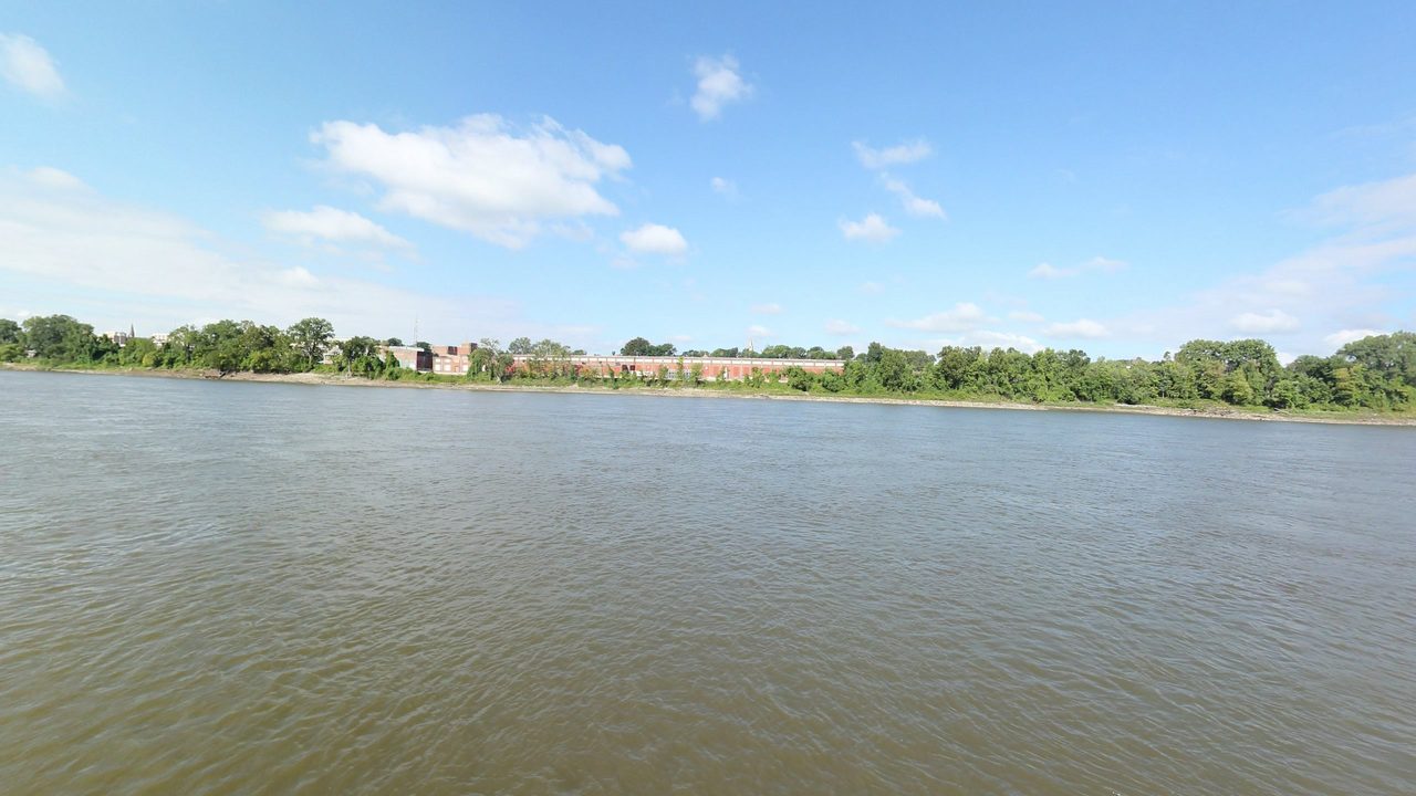 The Missouri River below a wooded far bank, with old brick buildings and a church steeple beyond, 2023