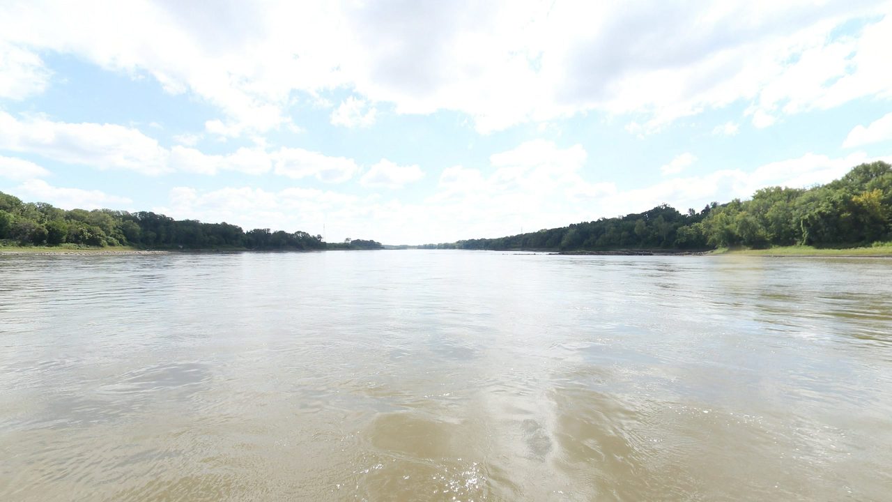 The Missouri River between long wooded banks under white clouds, 2023