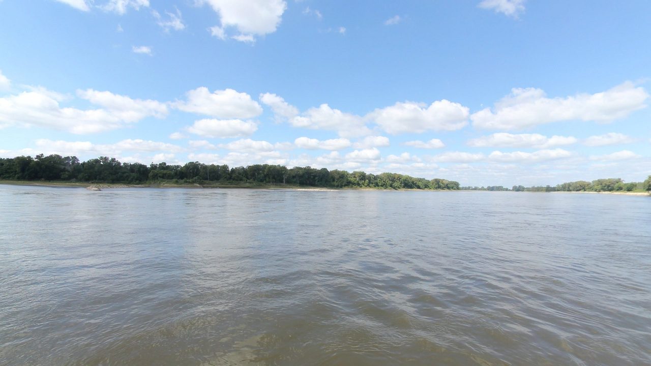 A wide, calm river under rows of white clouds, with a low wooded far shore, 2023
